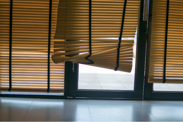 Partially raised wooden blinds covering a window with bright light behind them