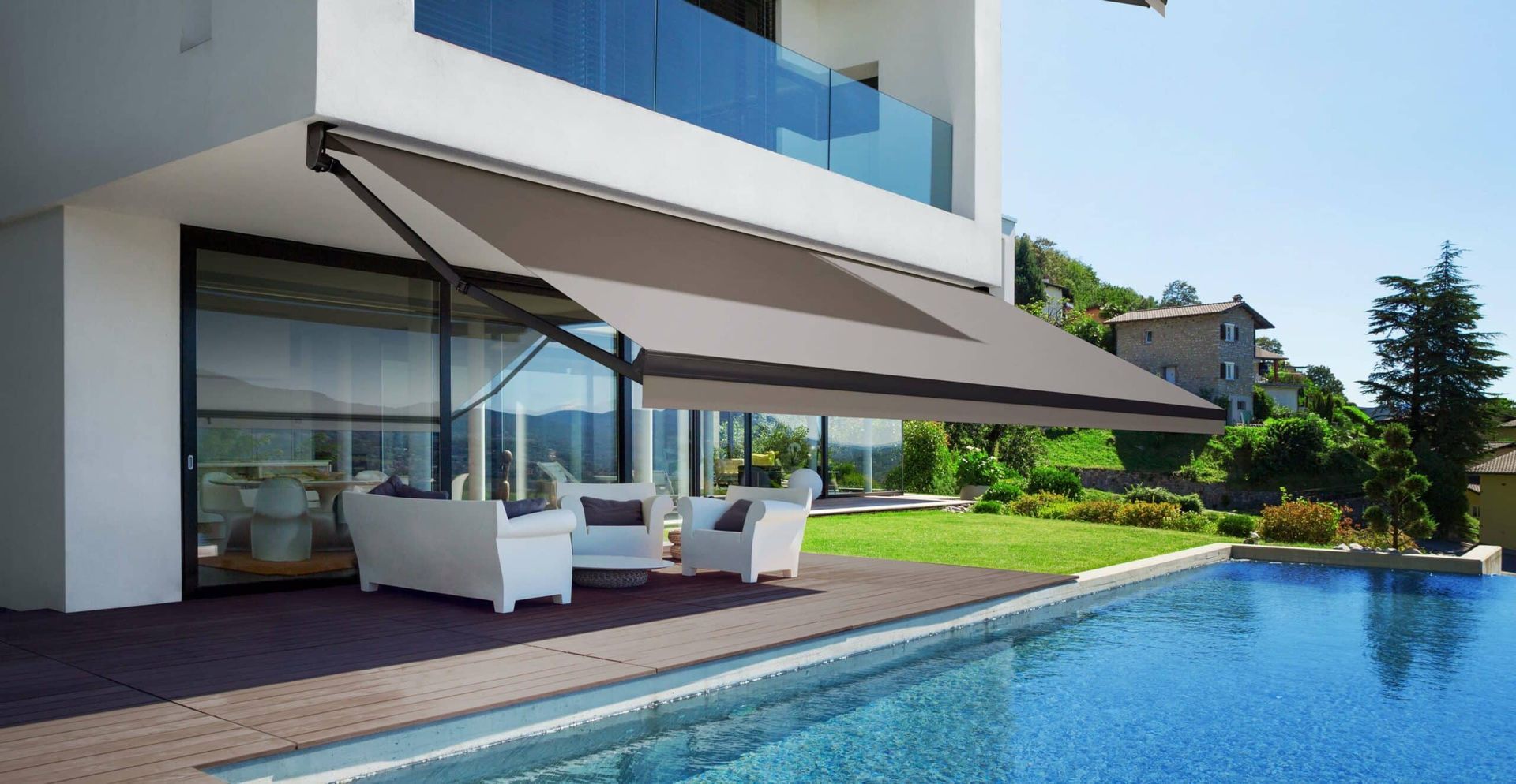 Modern house patio with white lounge chairs beside a swimming pool and retractable awning