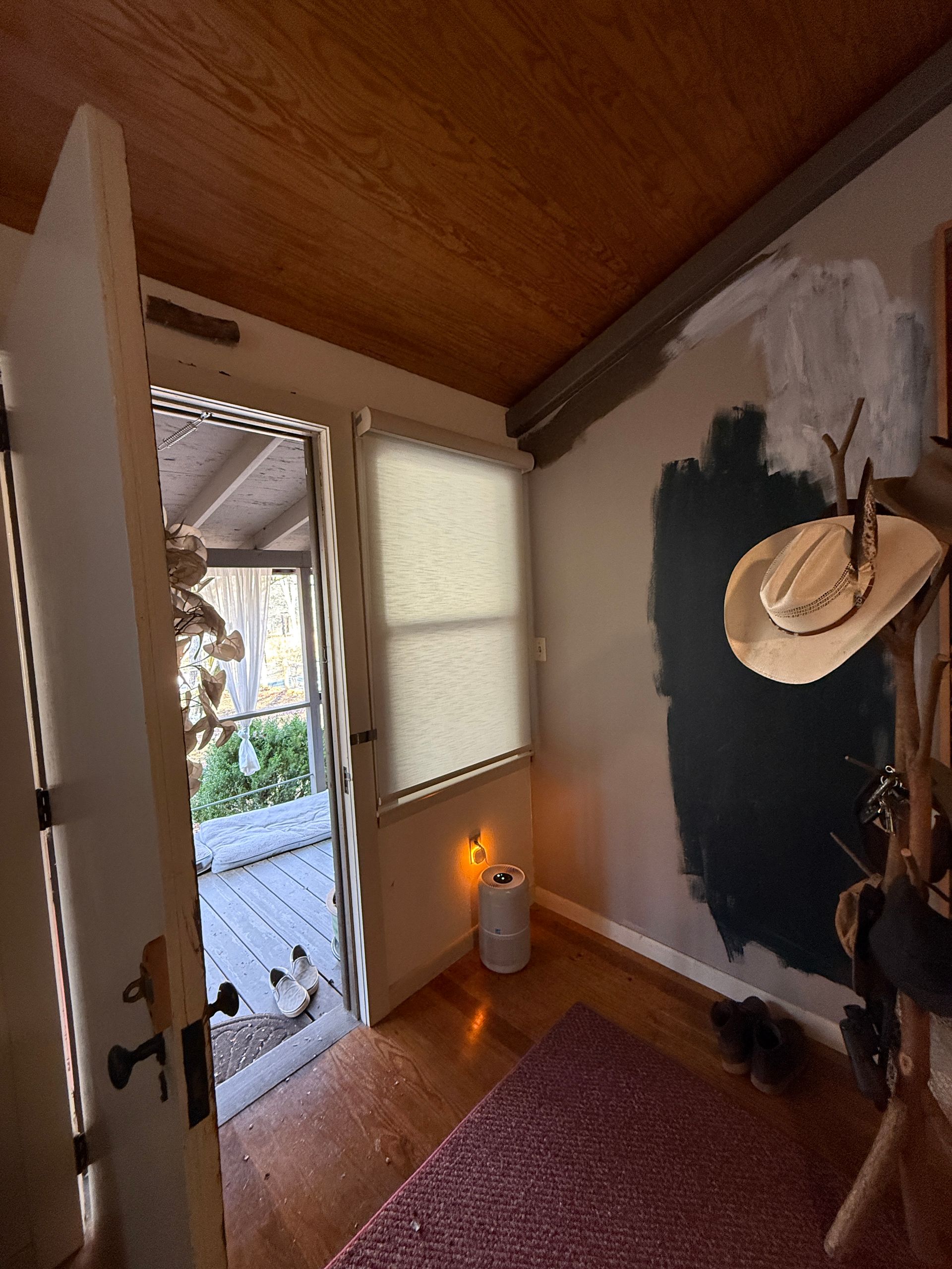Small entryway with open door, hat on wall, dark accent wall, and warm wood ceiling.