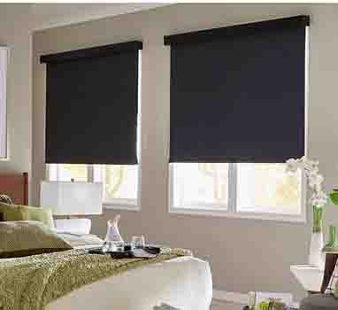 Bedroom with two windows covered by dark roller shades and a bed with green bedding in the foreground