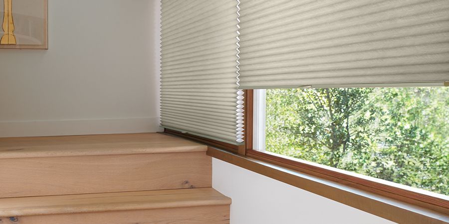 Minimalist room corner with light wood steps, white blinds, and a sunlit window view of greenery
