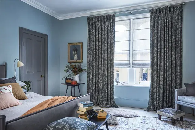Bright bedroom with blue walls, large window, bed, dresser, and patterned curtains