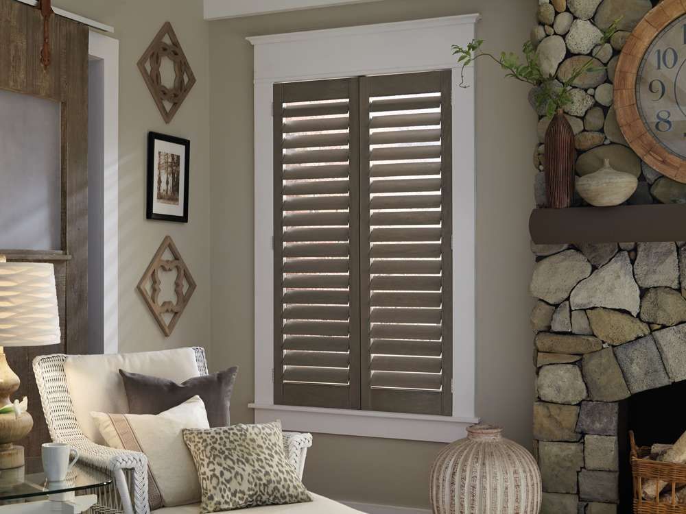 Cozy living room corner with window shutters, patterned pillows, and a stone fireplace