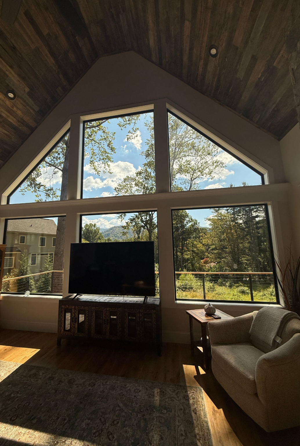 Living room with a large triangular window, TV, beige chair, and sunlight streaming in.