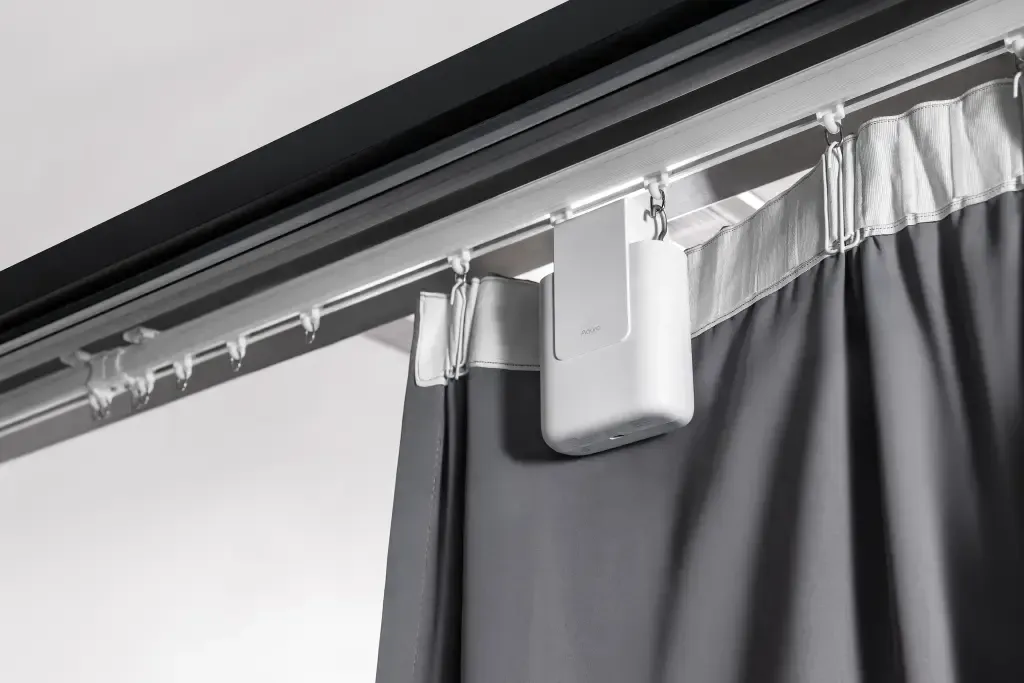 Curtain track with white hooks and a gray curtain hanging by a window