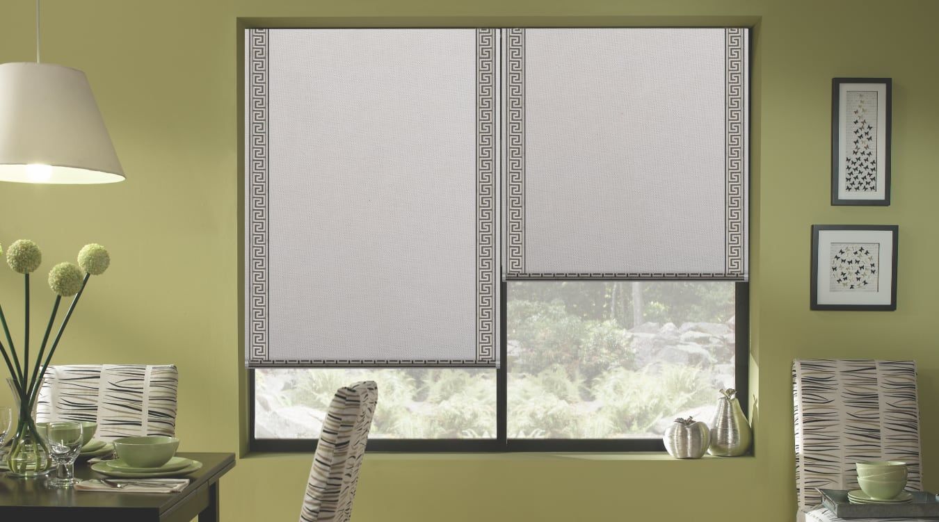 Muted green room with patterned window blinds, desk lamp, chair, side table, and framed wall art.