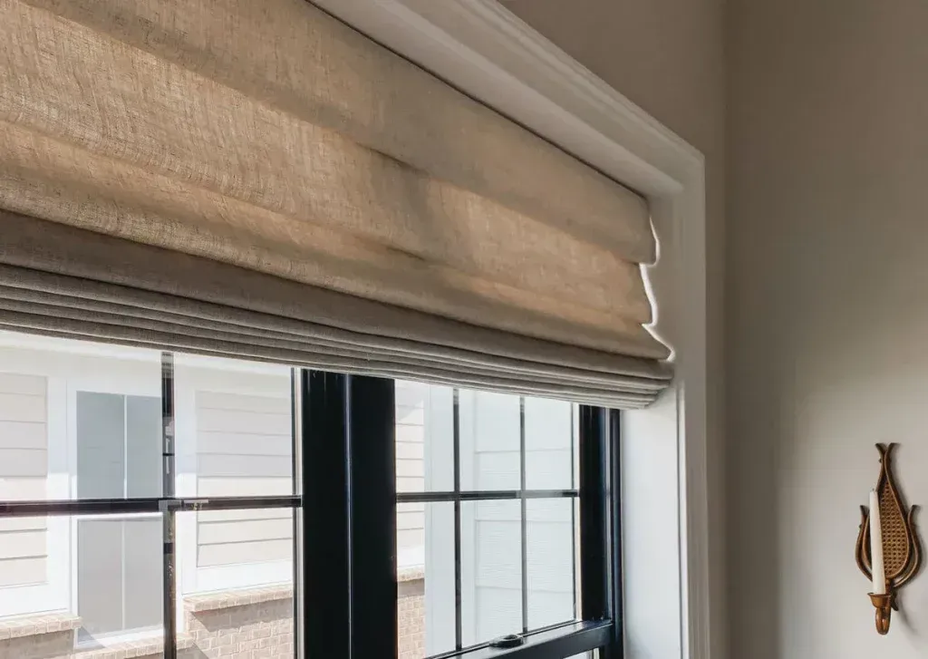 Beige Roman shade above a black-framed window in a bright room