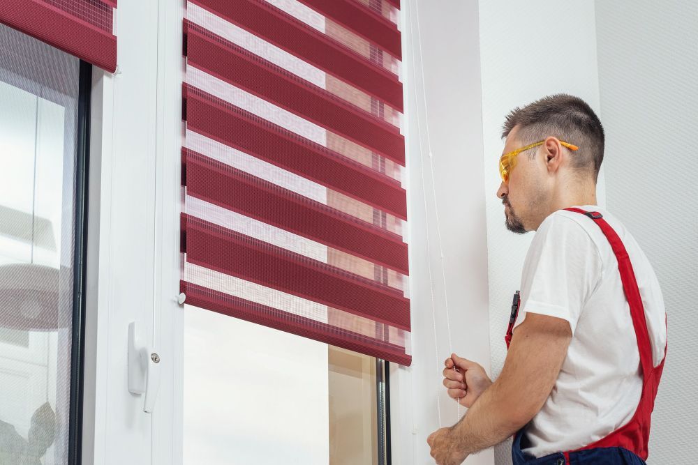 Worker installing red window blinds beside a white window