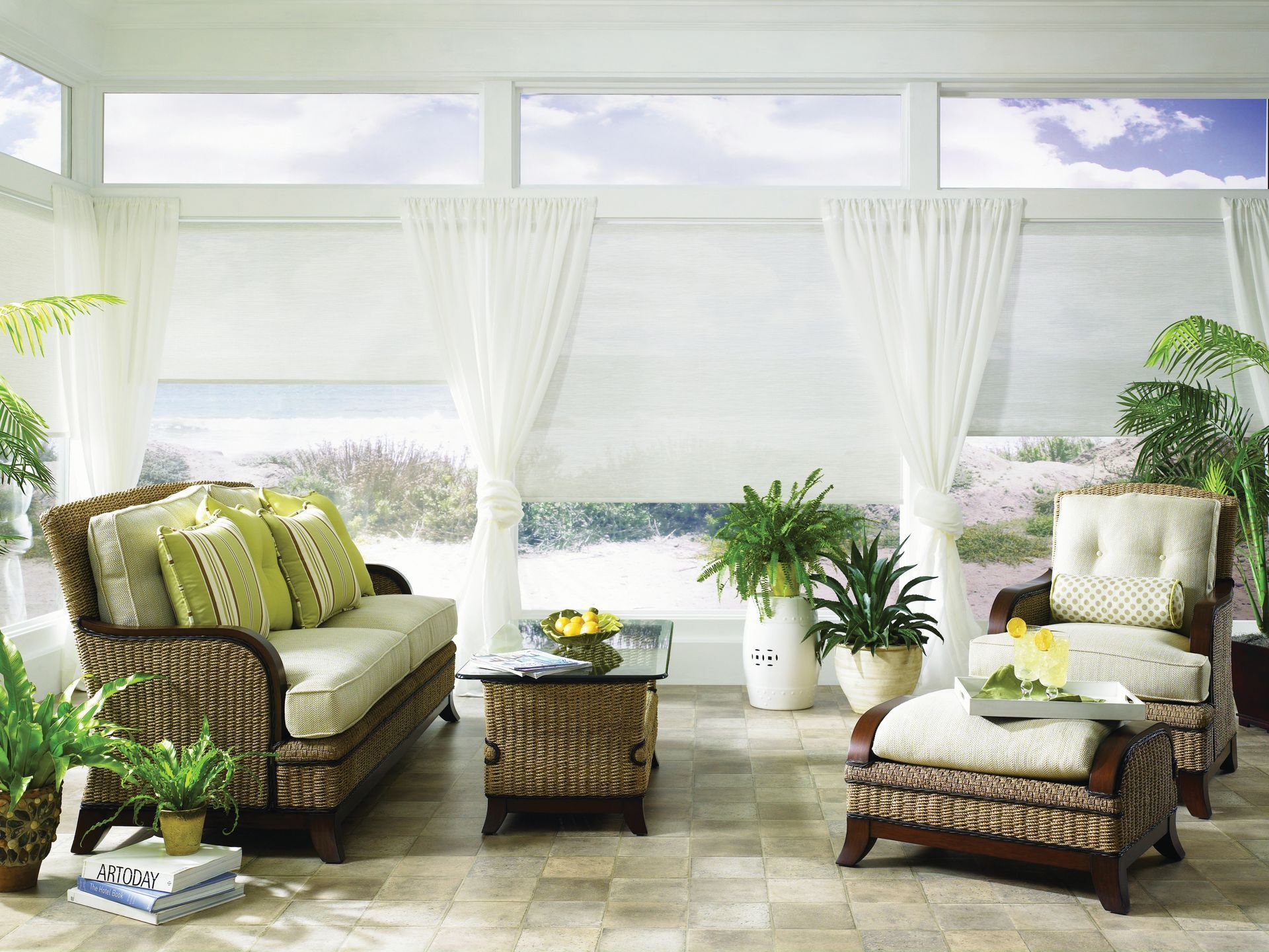 Bright sunroom with wicker patio furniture, green cushions, and ocean view through large windows