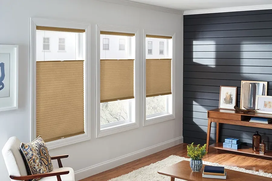 Bright living room with three windows, woven shades, and a wooden desk beside a dark accent wall