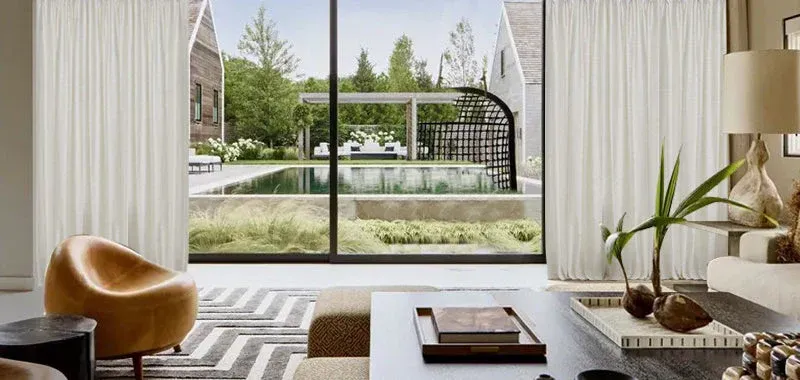 Bright living room with a large window overlooking a garden patio and pool, with modern furniture and decor