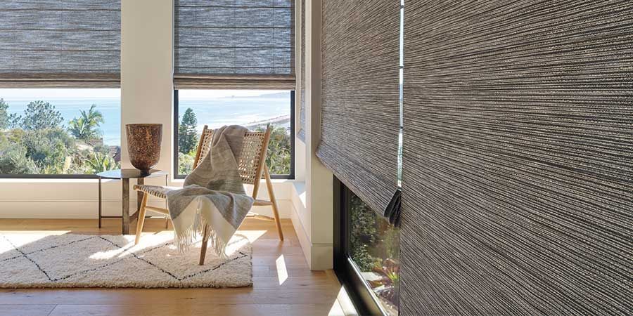 Sunlit modern living room with woven blinds, chaise lounge, chair, and ocean view through large windows