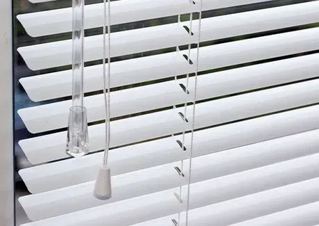 White window blinds with hanging pull cords closed over a window