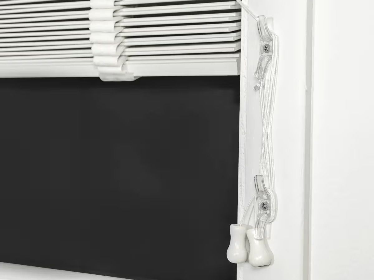 White blinds over a dark window with dangling pull cords on the right