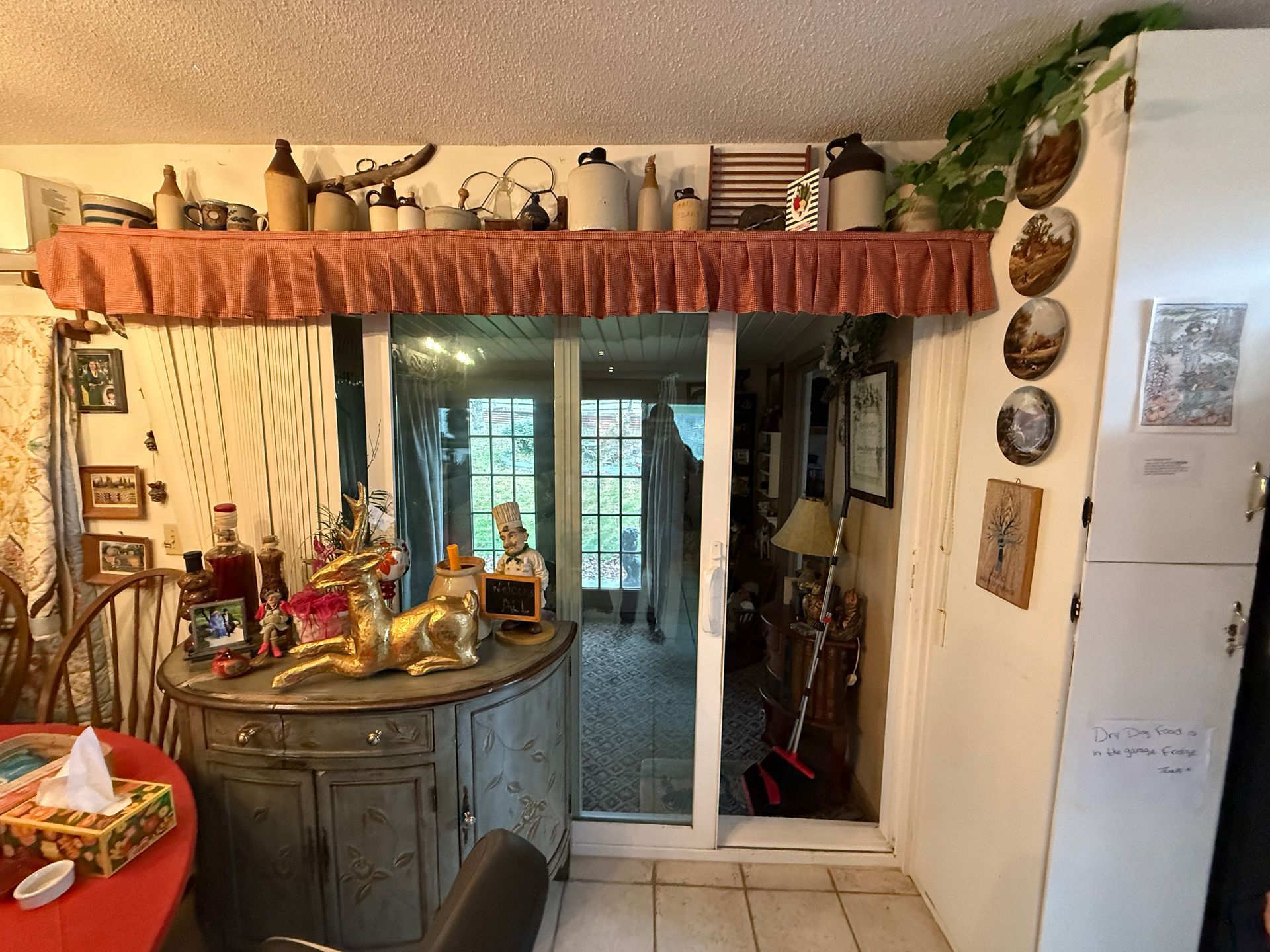 A cluttered interior with a view through a sliding door to an outside space. A variety of decor on display.