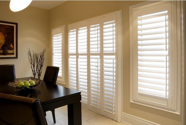 Dining room with dark table and chairs beside large windows with white plantation shutters