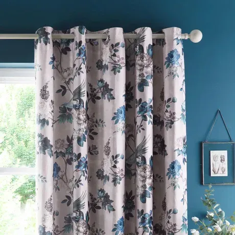 Floral curtains hanging on a window beside a blue wall and framed art piece