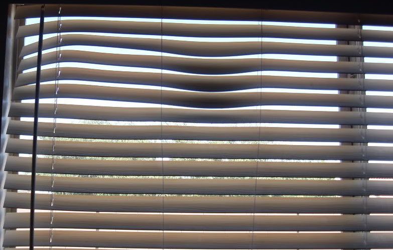 Closed window blinds with daylight peeking through the slats.