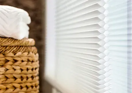 White window blinds beside a woven wicker basket with folded towels