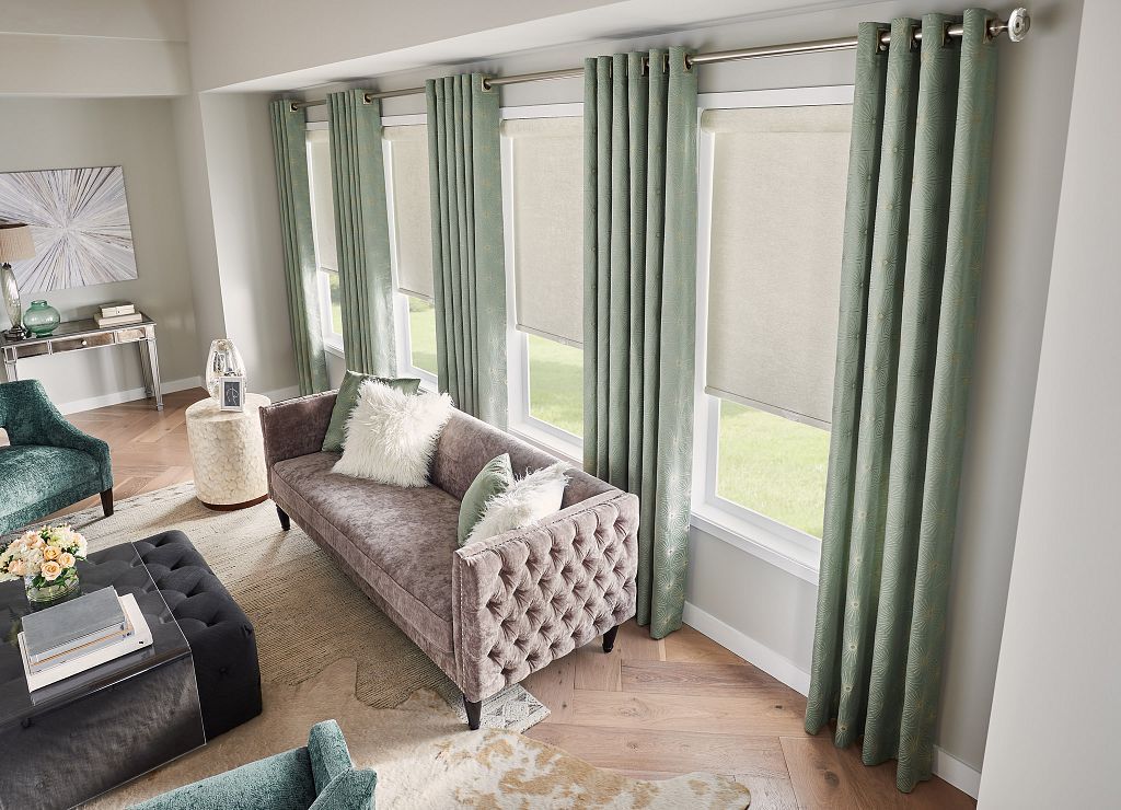 Bright living room with mint curtains, gray sofa, and dark tufted ottoman by a large window
