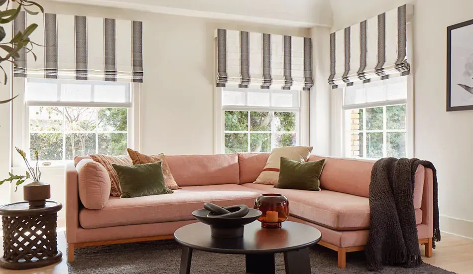 Bright living room with a pink sectional sofa, striped window shades, and a round coffee table.
