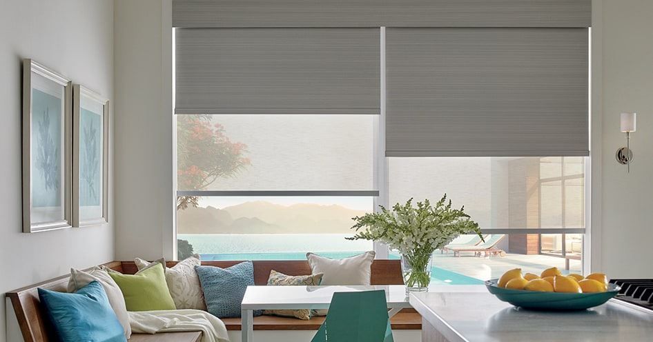 Bright modern living room with gray blinds, colorful sofa, and a dining table with flowers and fruit