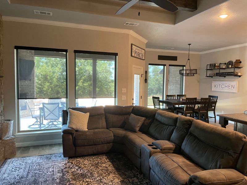 Roller shades in a comfortable living room with a dining room in the distance. Love is Blinds NC. 