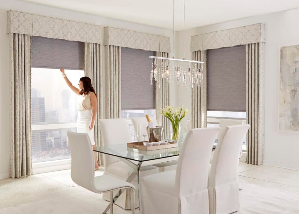 Bright dining room with glass table, white chairs, and a person adjusting window blinds