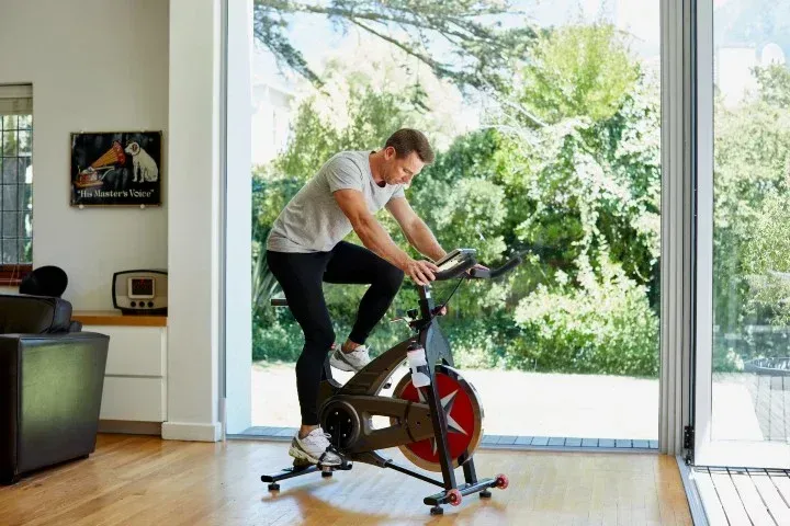 Person exercising on a stationary bike in a bright living room with large windows.