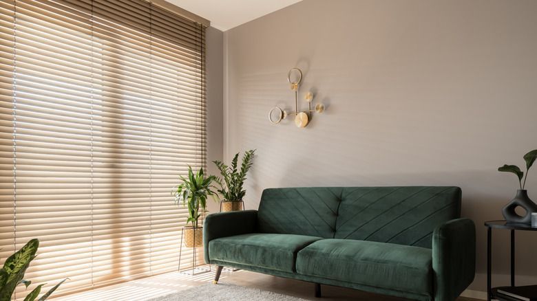 Bright living room with green sofa, large window blinds, potted plant, and wall sconce.
