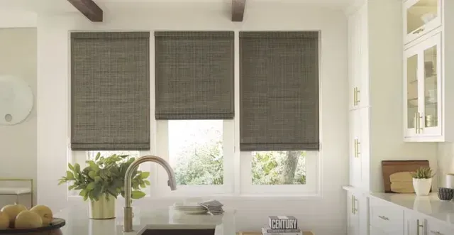 Modern kitchen with three gray window shades, sink, and white cabinets in soft natural light