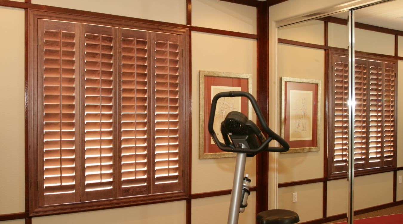Gym room with exercise bike in front of wood-paneled windows and framed wall art