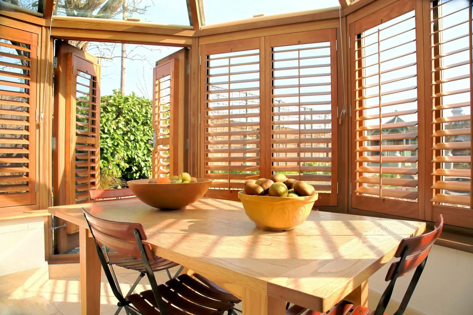 Sunlit dining nook with wooden shutters, round table, and bowls of fruit