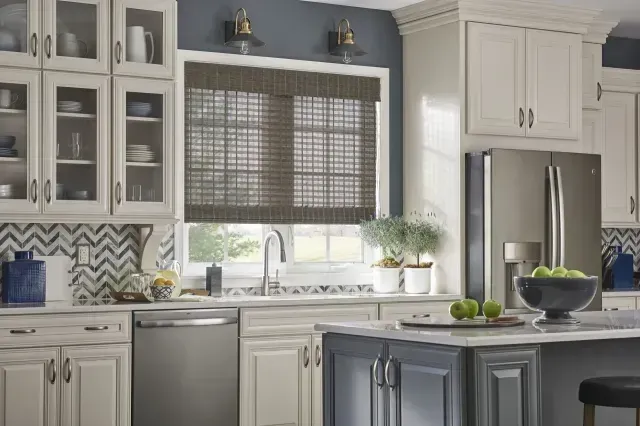 Bright modern kitchen with white cabinets, gray island, stainless fridge, and window with blinds