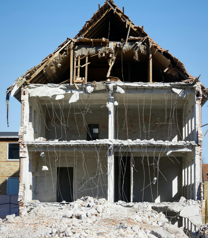 A partially demolished two-story house with its interior exposed to the outdoors, surrounded by debris.