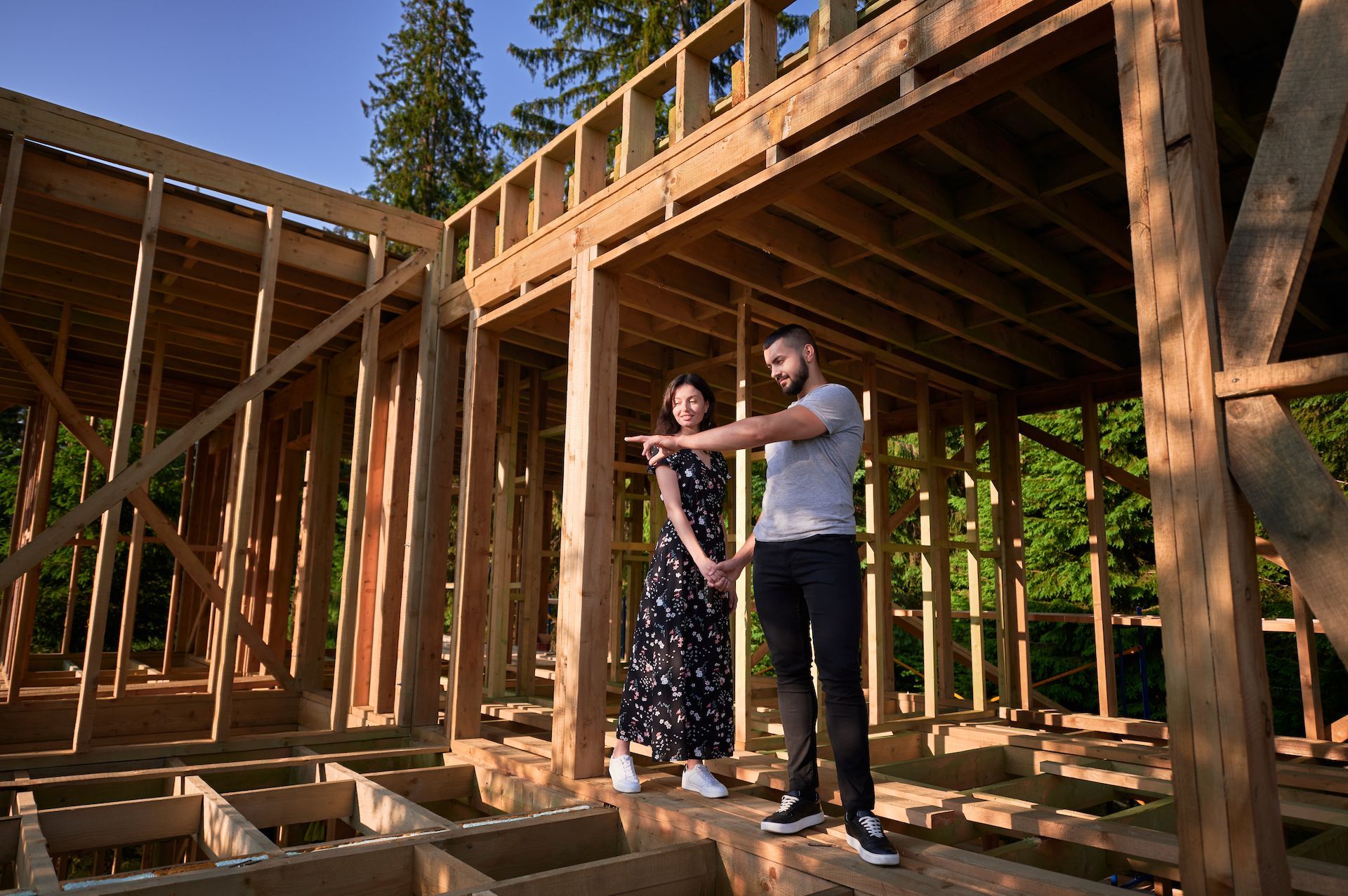 A man and a woman are standing in front of a wooden house under construction.