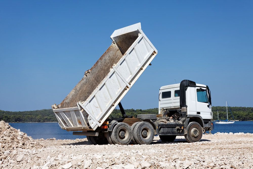 A Dump truck is Sitting on top of a Rocky Beach next to a body of Water — Ian Brown Sand Supplies and Tipper Hire In Port Macquarie, NSW