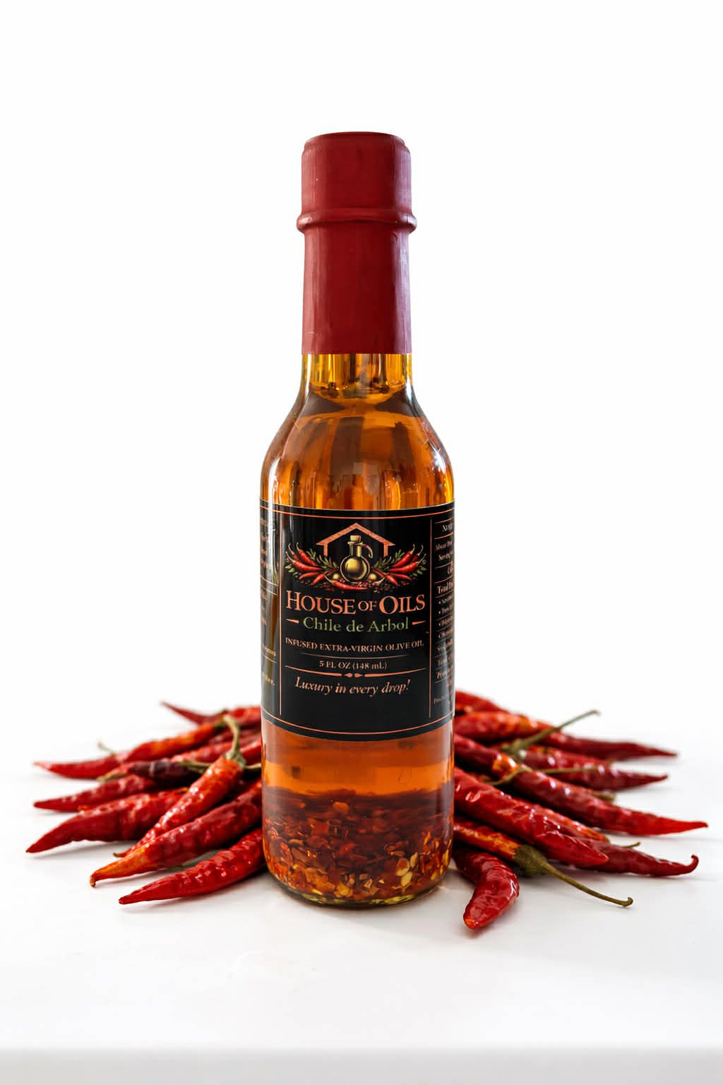 Bottle of chili sauce with red peppers arranged around it on a white background
