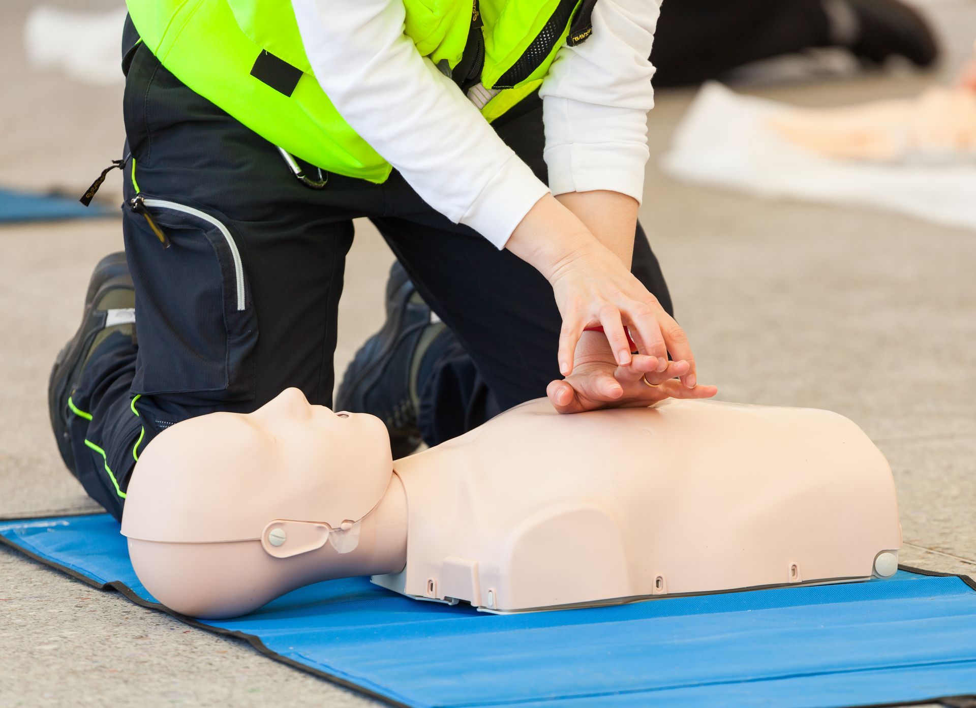 Person performing CPR chest compressions on a CPR training mannequin on a blue mat