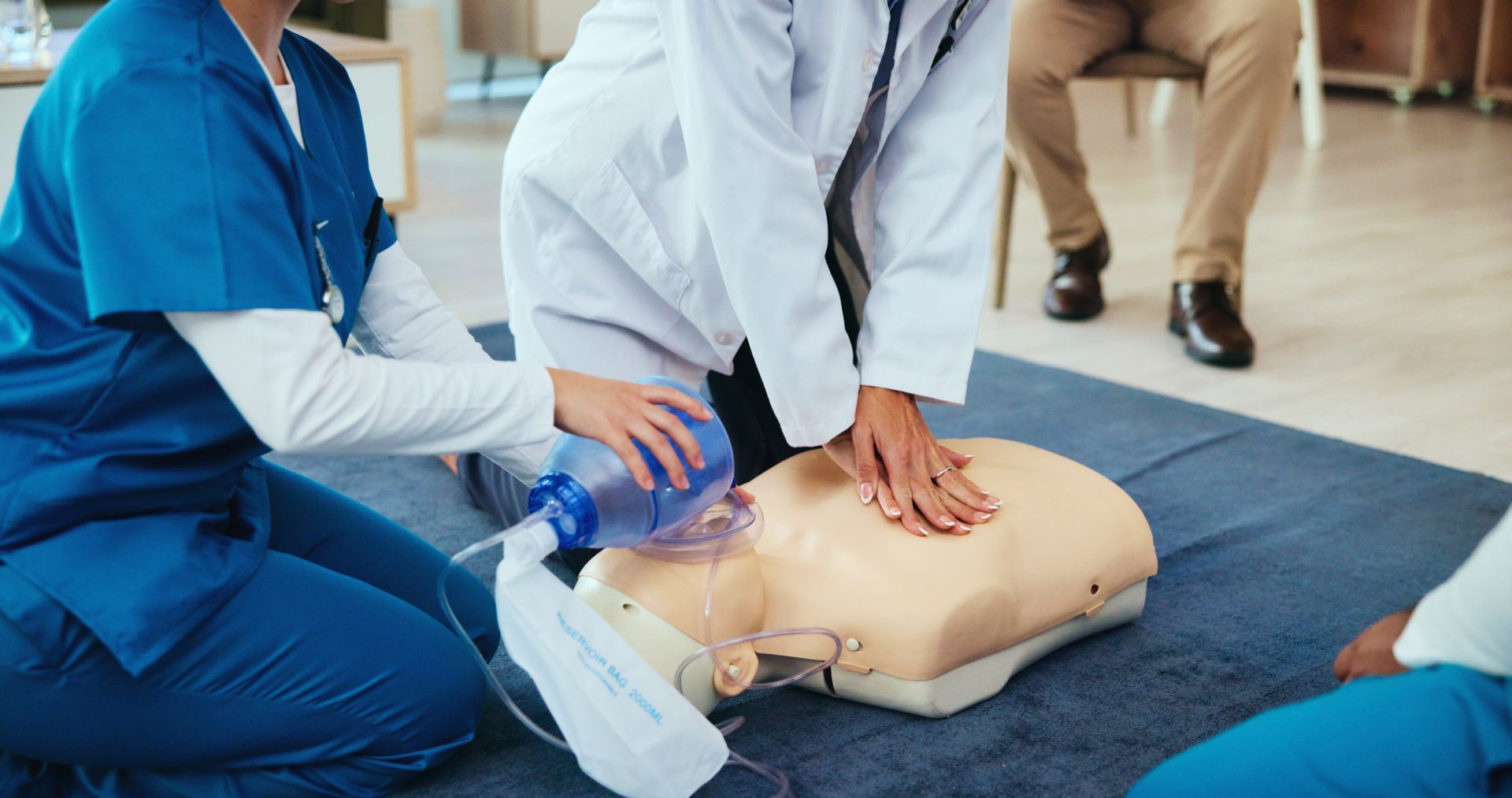 CPR training on a mannequin with two responders in scrubs
