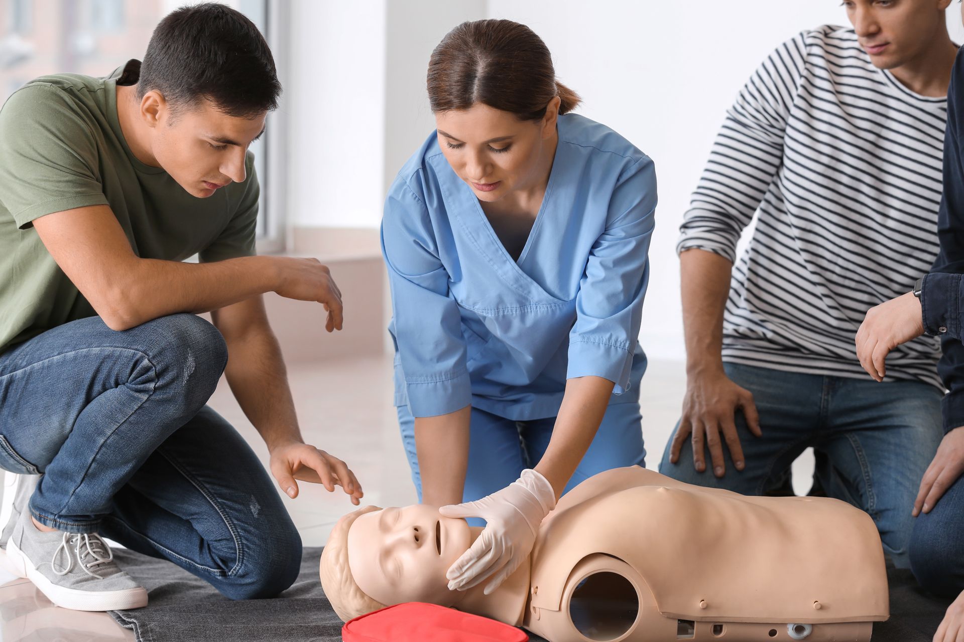 Three people practicing CPR on a training mannequin on the floor