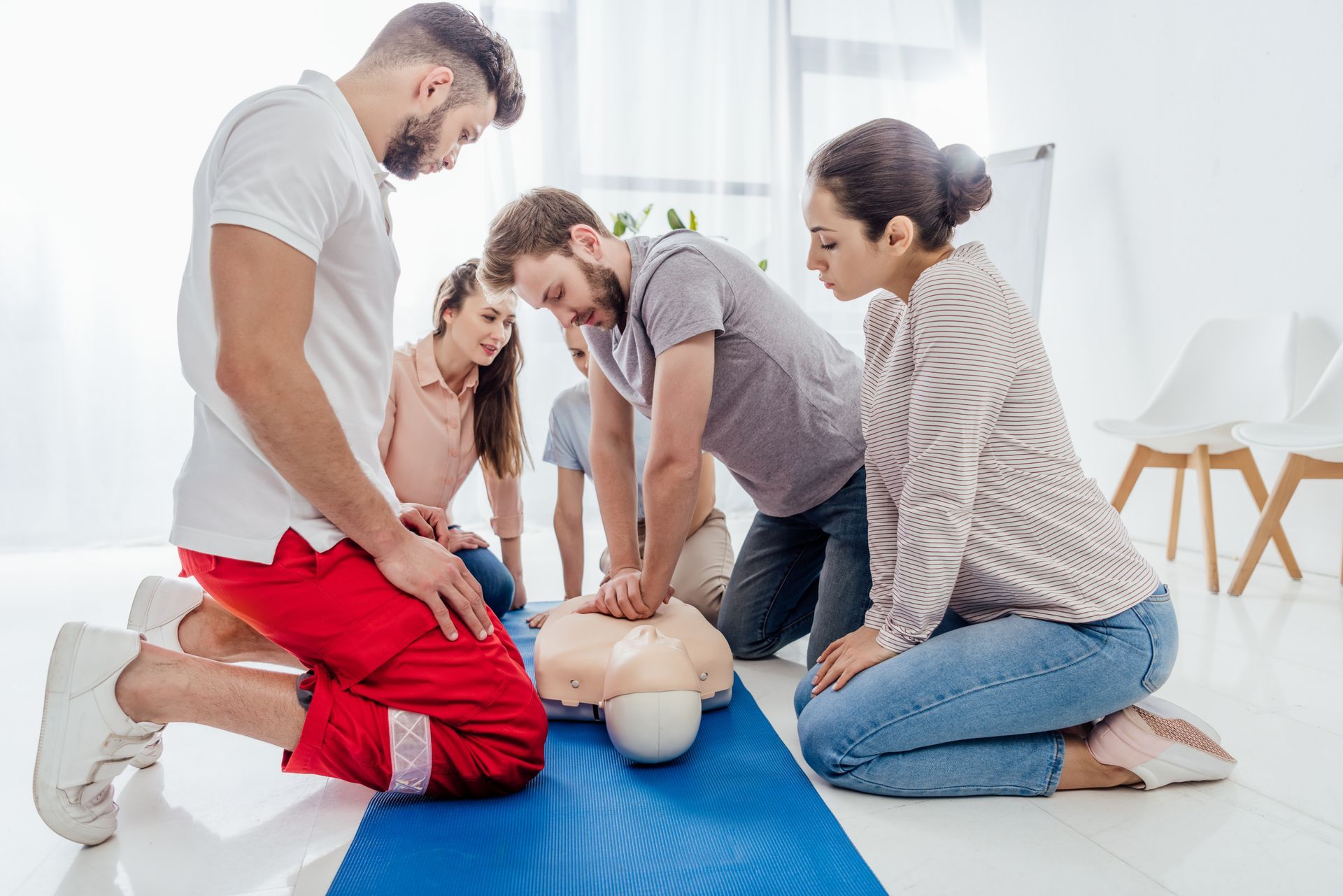Group practicing CPR on a training manikin in a bright room