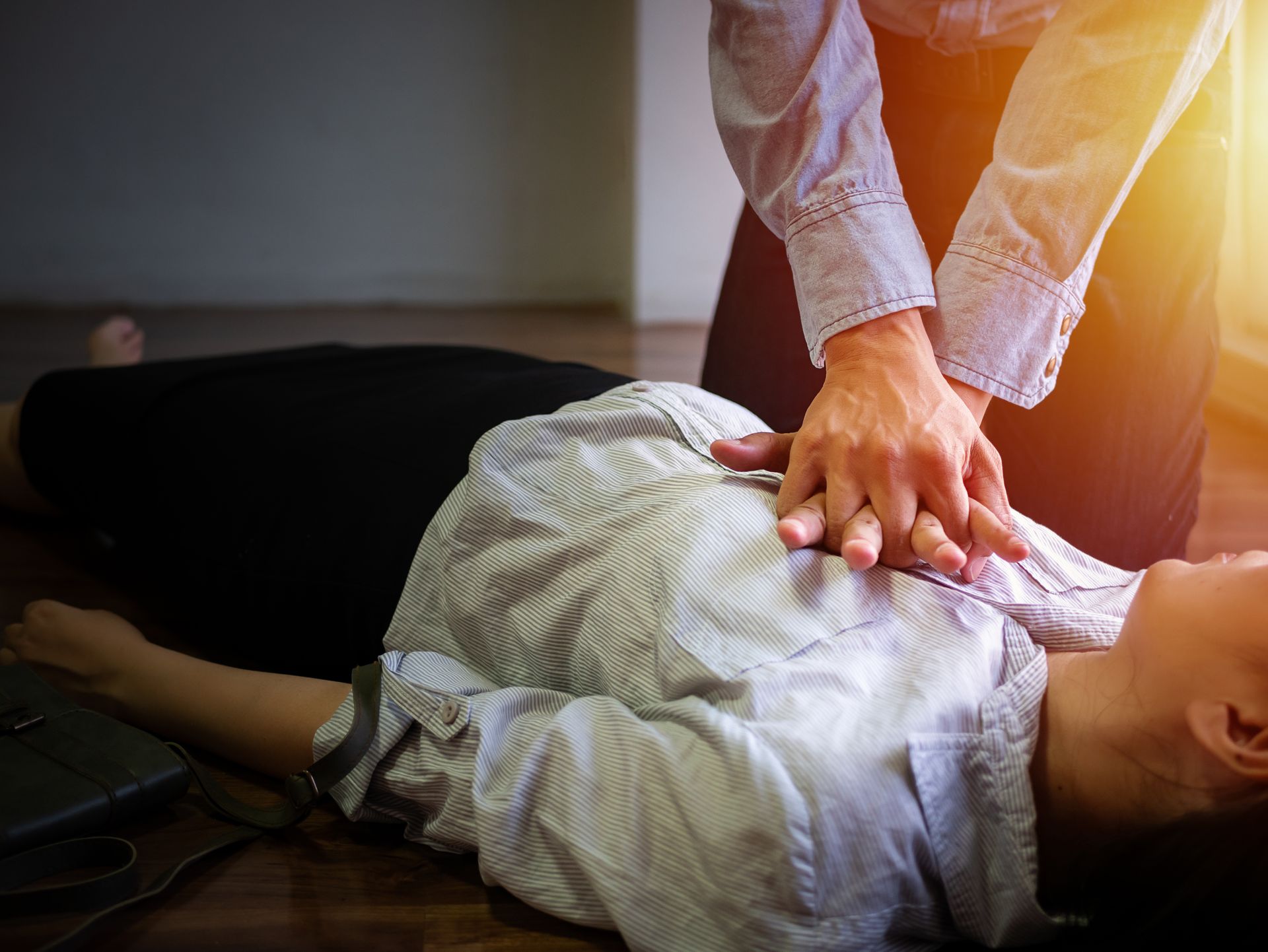 Person giving chest compressions during CPR on a woman lying on the floor