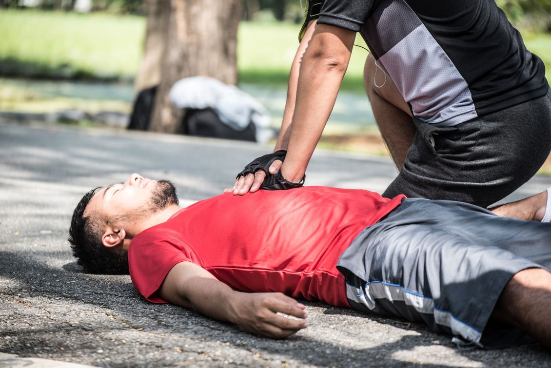 Person lying on pavement while another person kneels beside them, checking for a pulse or responsiveness