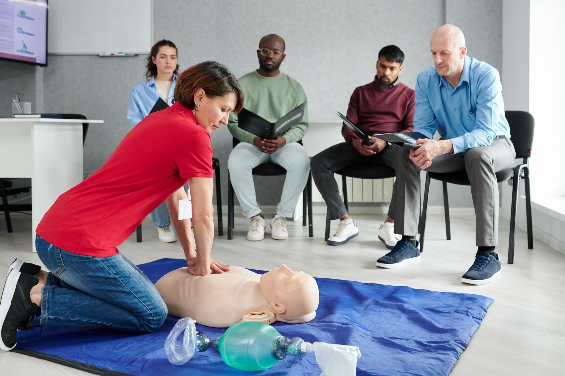 CPR training session with instructor performing chest compressions on a mannequin while others observe