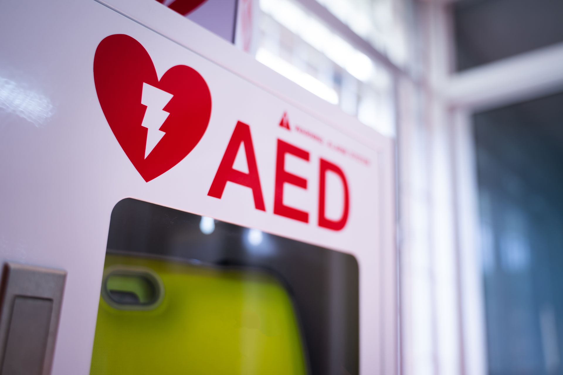 Red AED sign above a wall-mounted defibrillator cabinet