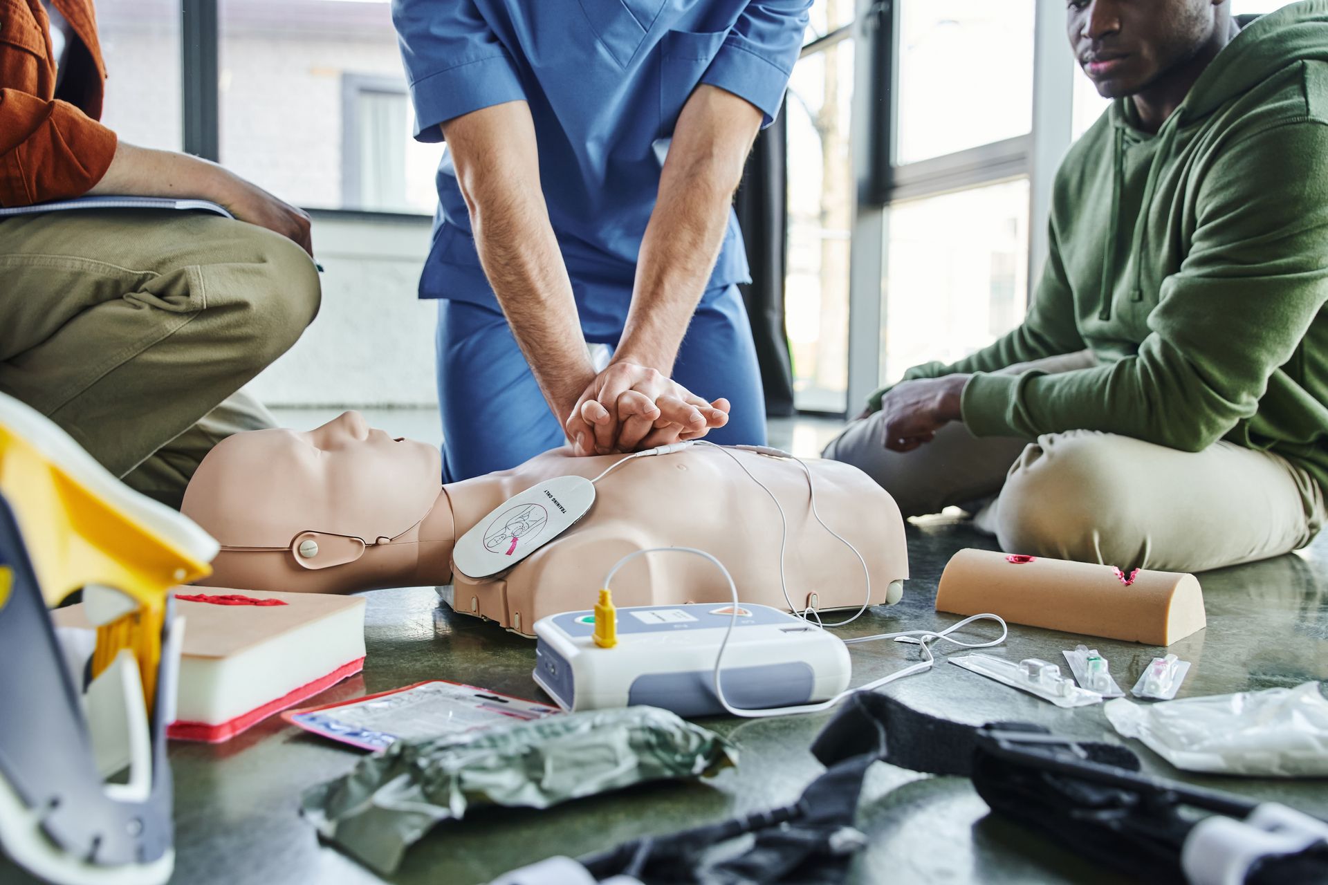 People performing CPR training on mannequins with first aid supplies on the floor