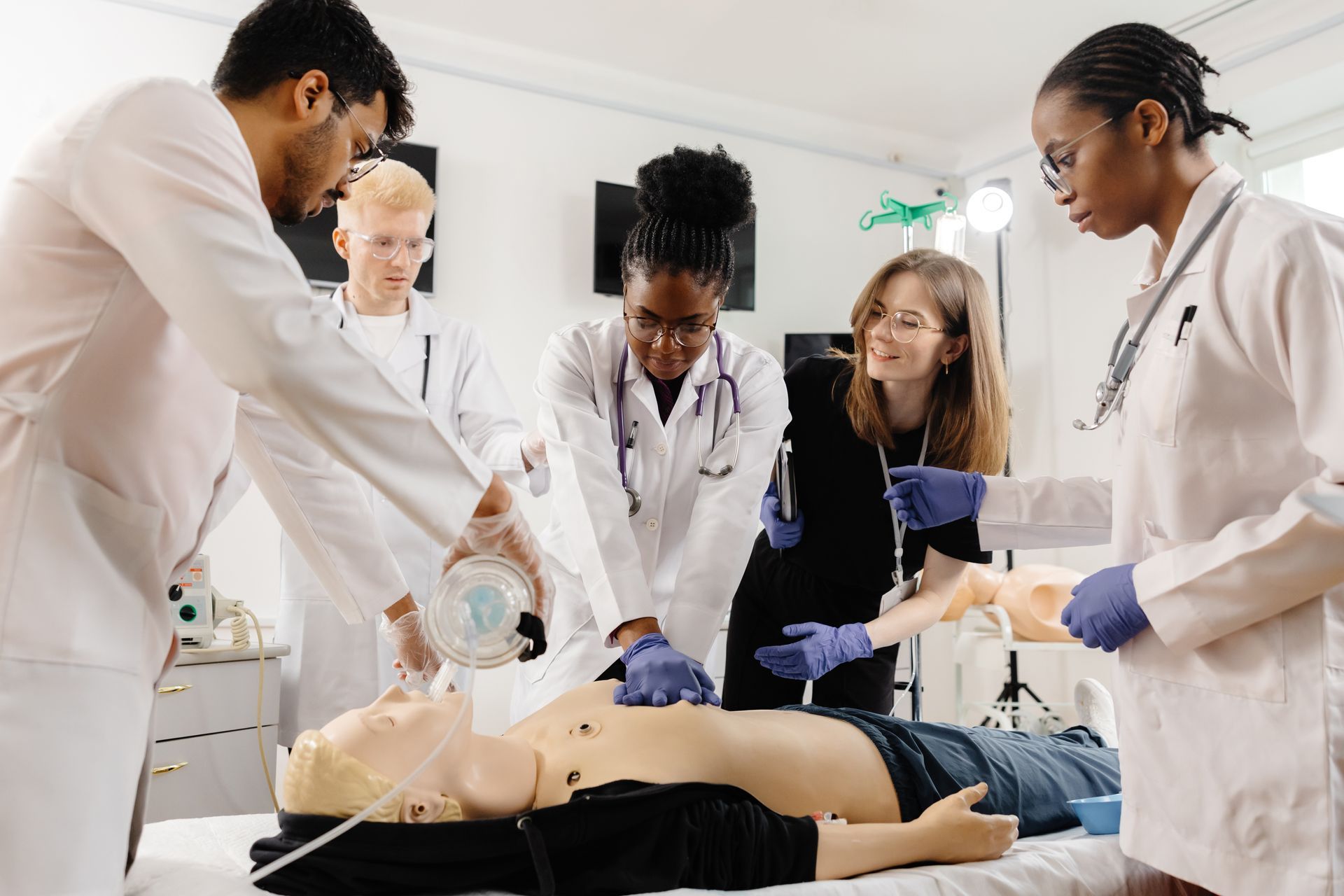 Medical students practicing CPR on a training mannequin in a bright classroom