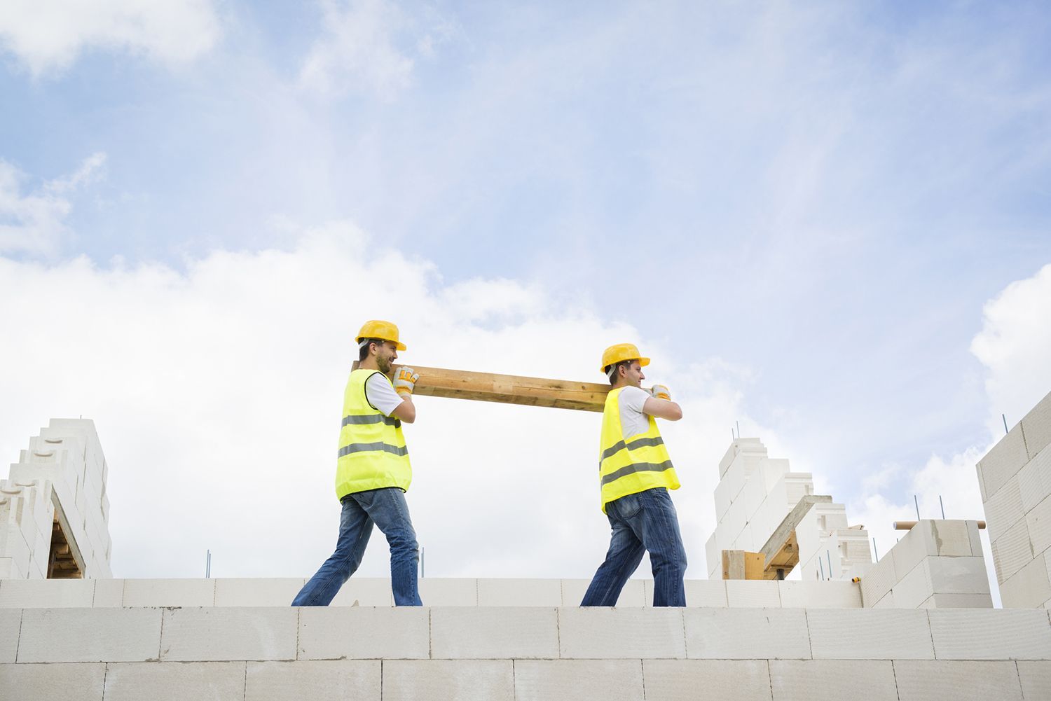 Two construction workers are carrying a large piece of wood.