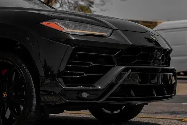 Black Lamborghini Urus SUV front view, showing grill, headlight, and wheel.